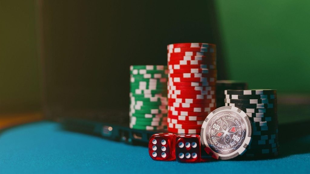 A close-up of poker chips and red dice on a blue felt gaming table, with stacks of red, green, and black chips in the background